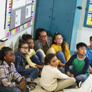 A diverse group of children and a teacher sitting on the floor in a classroom.