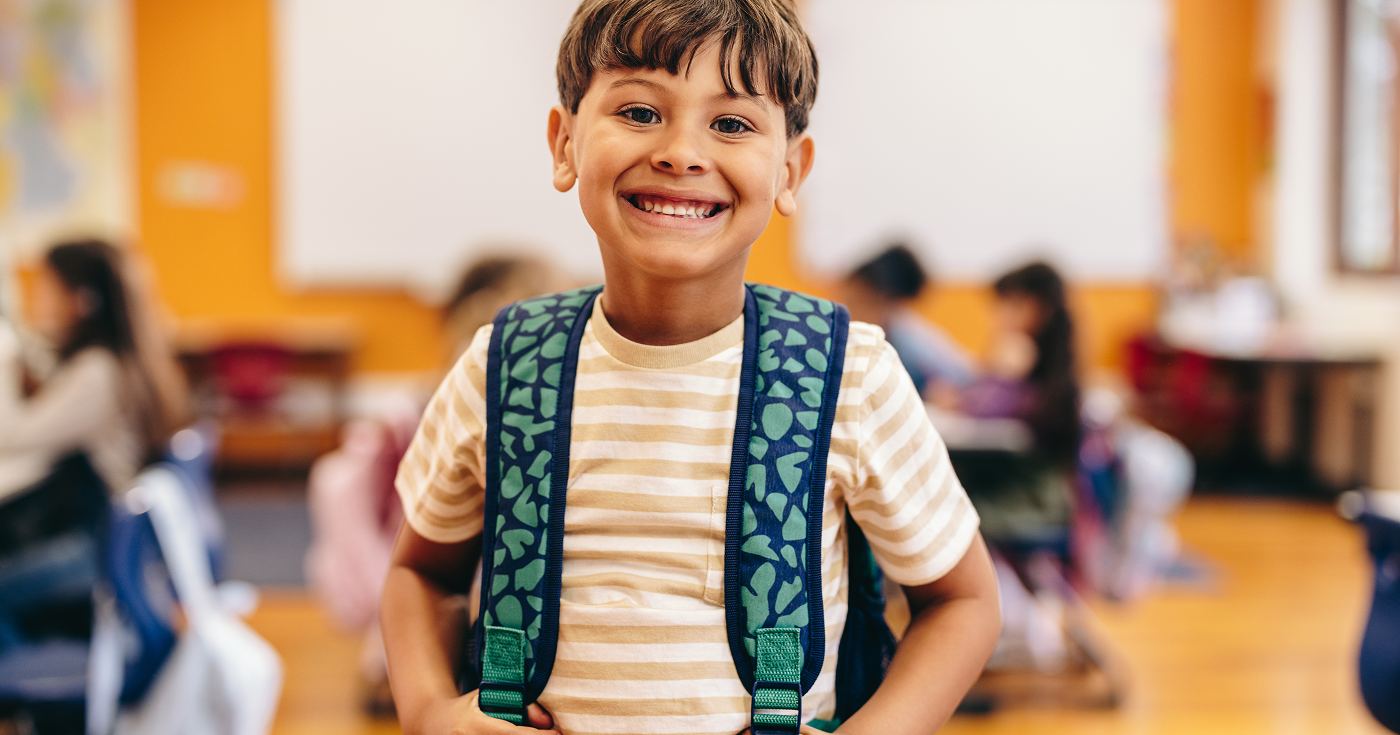 Smiling young boy with backpack ready for school.