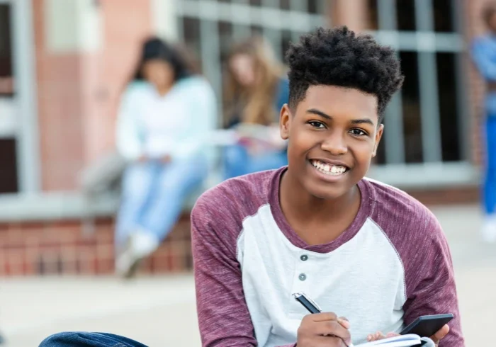 Boy sitting outdoors, holding a notebook